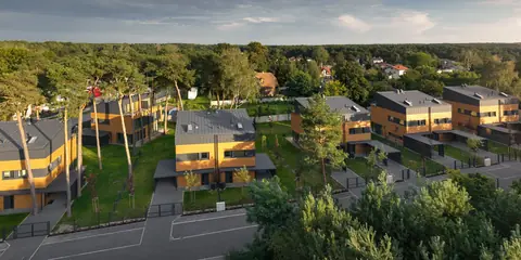 Panorama osiedla z lotu ptaka: sześć budynków, droga wewnętrzna i las w tle.